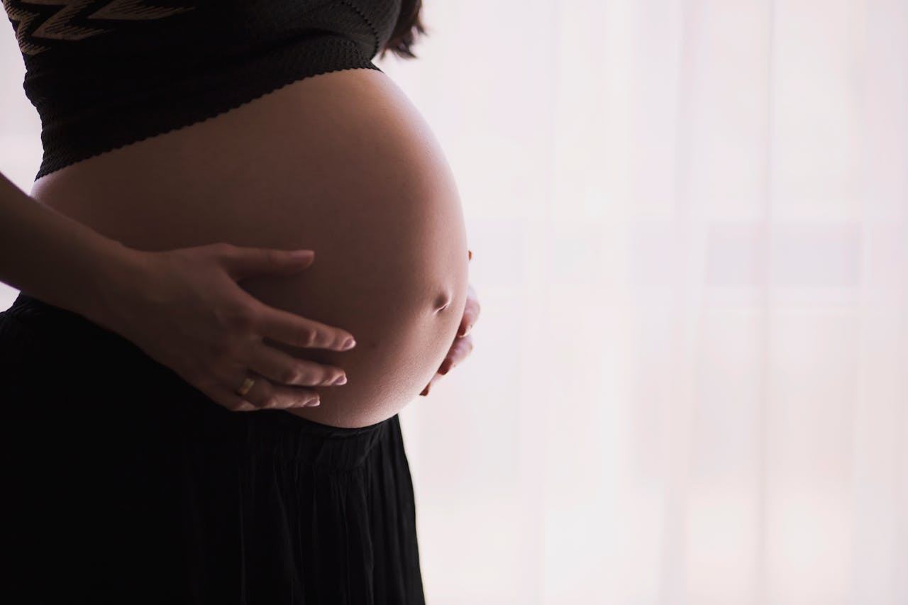 our-mission A close-up of a pregnant woman touching her bare belly, expressing warmth and care.