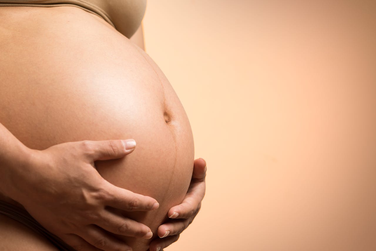 service-04 A tender close-up of a pregnant womans hands holding her belly, symbolizing maternity and love.